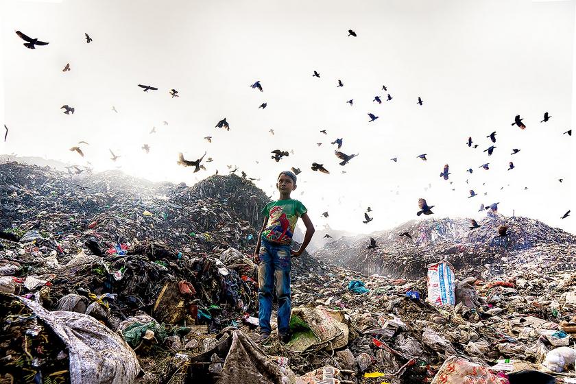 Ein Junge steht inmitten einer riesigen Mülldeponie. Im Hintergrund fliegen Vögel hoch