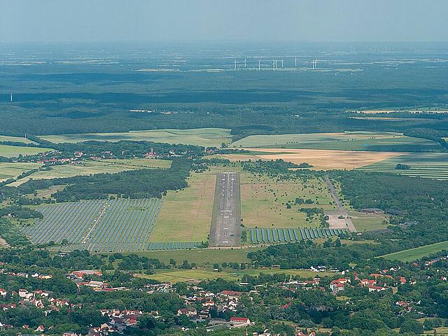 Luftaufnahme Flugplatz mit PV und Windkraftanlagen am Horizont