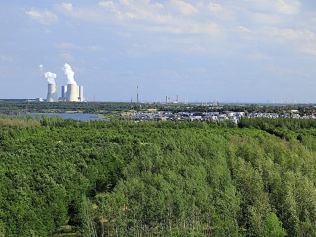 Kraftwerk mit Schornsteinen, daneben Windpark