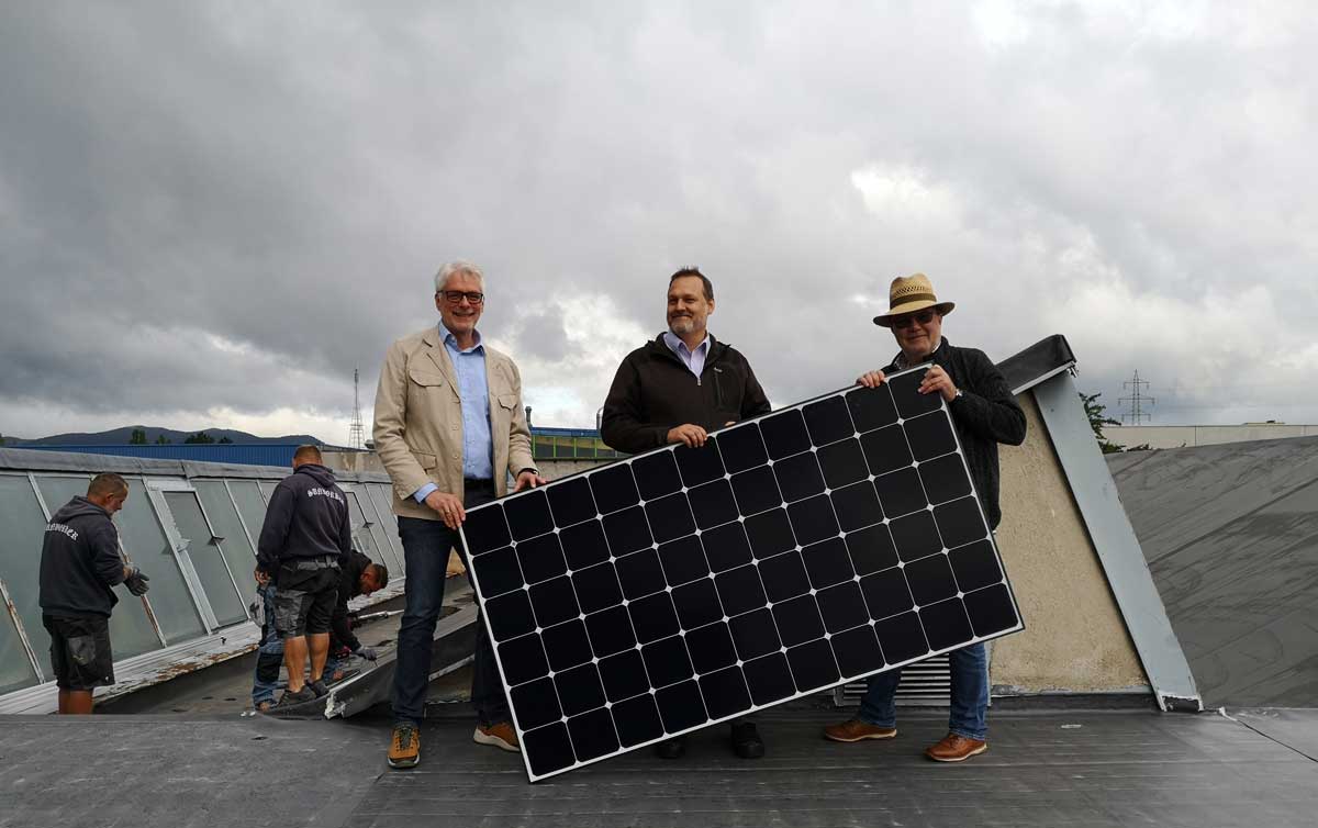 Drei Männer halten ein Solarmodul hoch