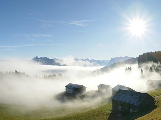 Bergwiese mit wenigen Häusern im Nebel