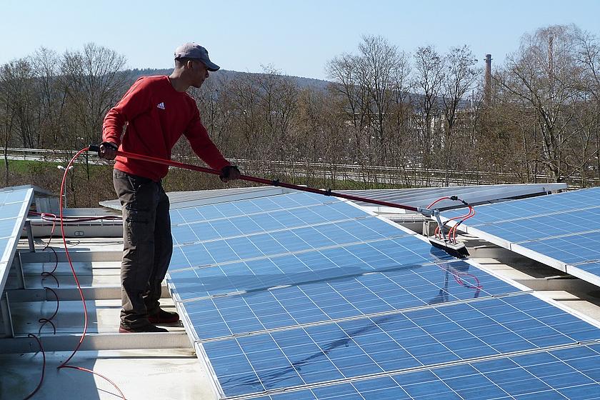 Arbeiter bei der Reinigung von Solarmodulen auf einem Dach