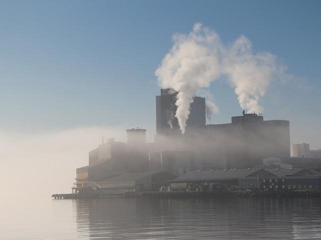 Industriebetrieb am Fjord in Norwegen im Nebel mit rauchenden Schloten