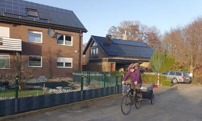 Mann auf einem Lastenrad vor Haus mit Solaranlage