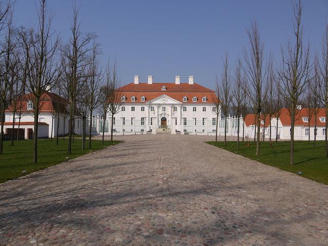 Auffahrt zu einem Schloss mit weißer Fassade und rotem Dach