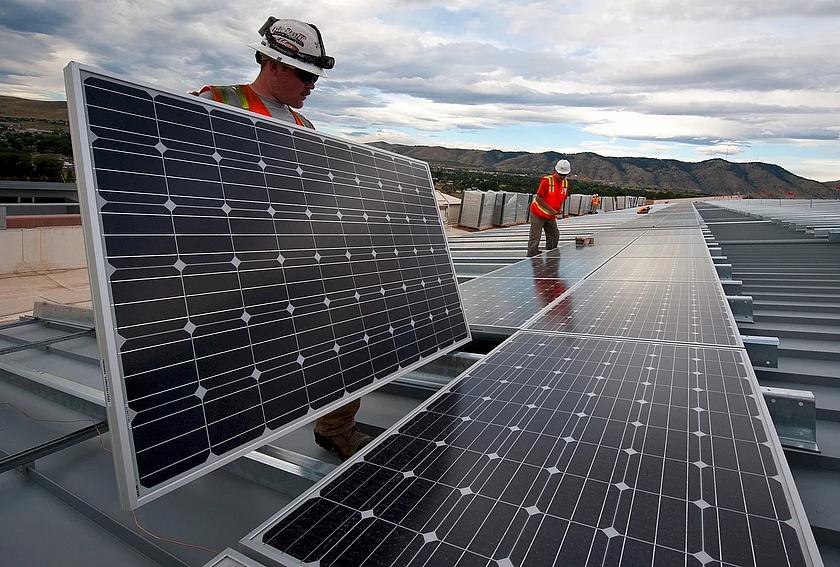 Ein Arbeiter hat ein großes Solarpanel in der Hand, was er im Begriff ist zu installieren auf einem Dach.