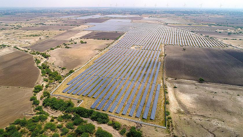 Luftbild eines riesigen Solarparks in Indien. Im Hintergrund sind auch Wndkrafträder zu sehen.