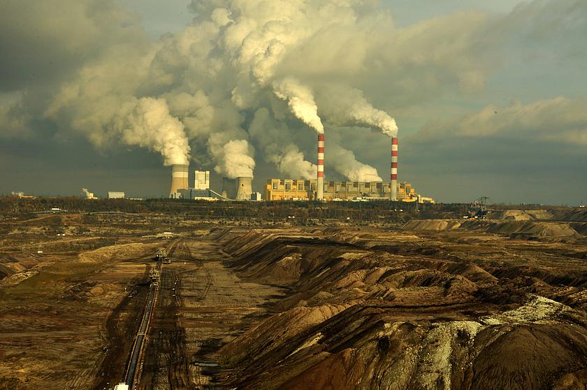 Bild Eines Kohlekraftwerks mit vielen rauchenden Schlöten. Davor eine Tagebaulandschaft.