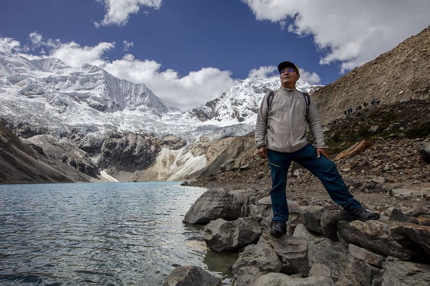 Ein Mann steht an einem Bergsee mit einem Gletscher im Hintergrund
