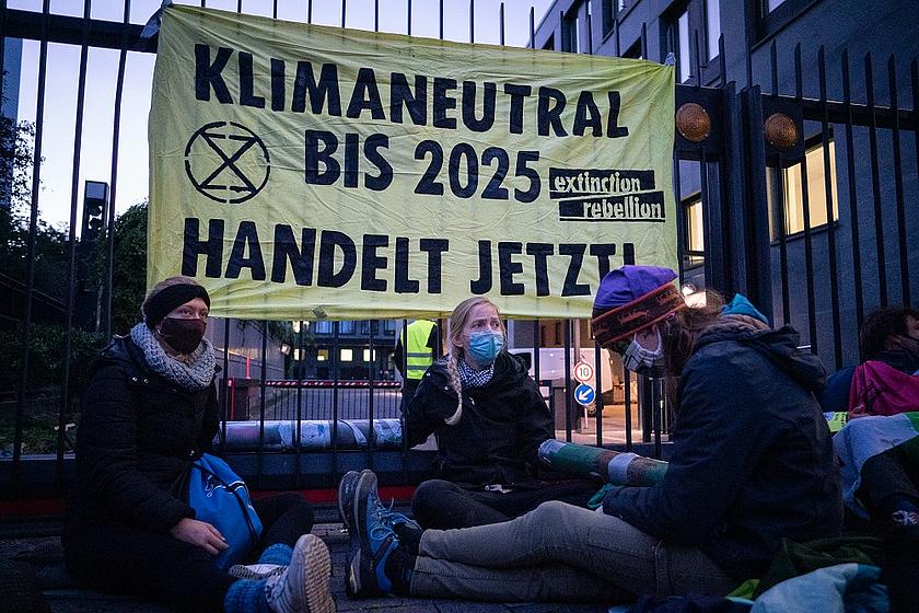 Aktivsten haben sich an ein Gitter angekettet. Hinter ihnen ein Transparent mit der Forderung nach Klimaneutralität bis 2025.
