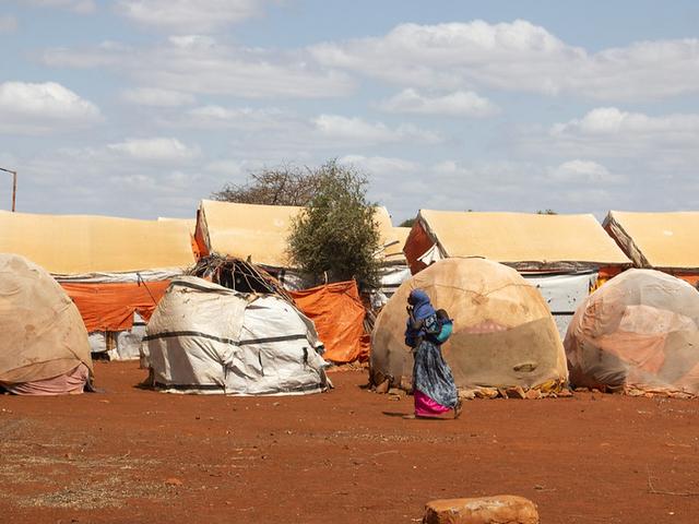 Eine Frau mit Kind läuft an einem Flüchtlingscamp mit Zelten entlang