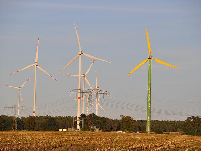 Mehrere Windräder, eines davon mit grünem Mast