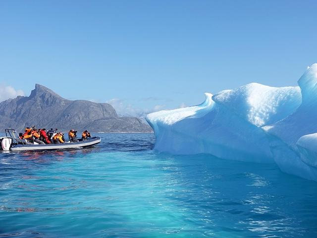 Großes Schlauchboot mit Touristen, die einen im Wasser treibenden Eisberg fotografieren