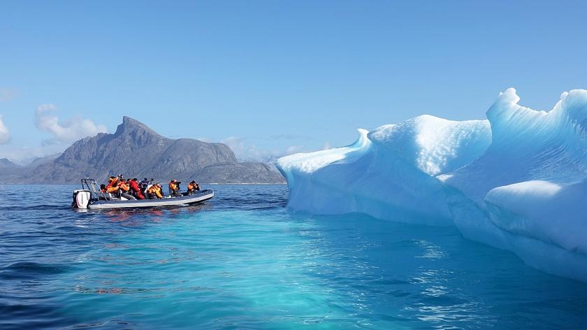 Großes Schlauchboot mit Touristen, die einen im Wasser treibenden Eisberg fotografieren