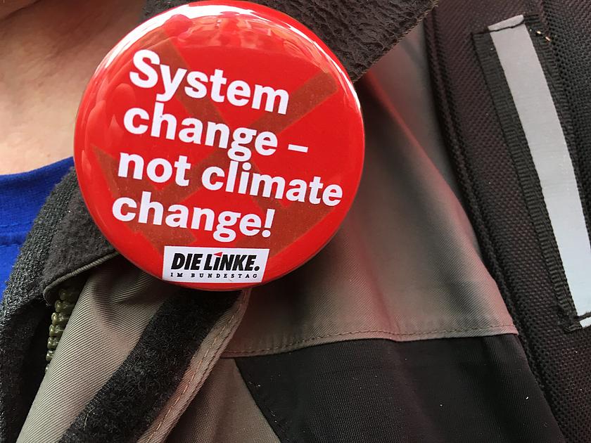 Button auf einer Jacke in Nahaufnahme. Auf diesem steht: "System Change, not Climate Change - DIE LINKE im Bundestag."