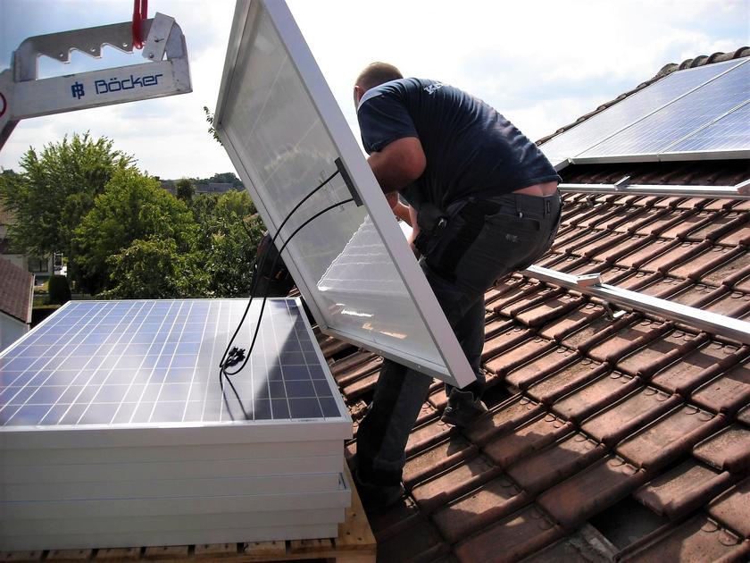 Mann installiert Solarmodule auf einem Hausdach