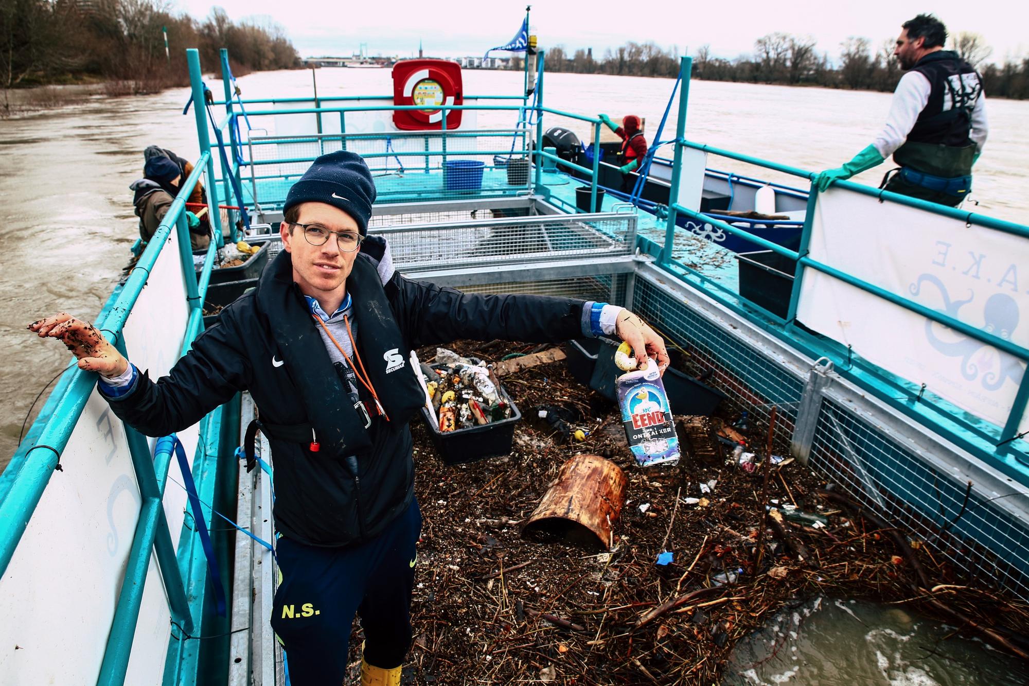 Ein Mann auf einem Schiff, voll mit Müll, hält eine Plastikflasche in der Hand