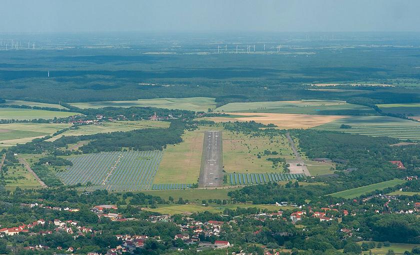 Luftaufnahme Flugplatz mit PV und Windkraftanlagen am Horizont