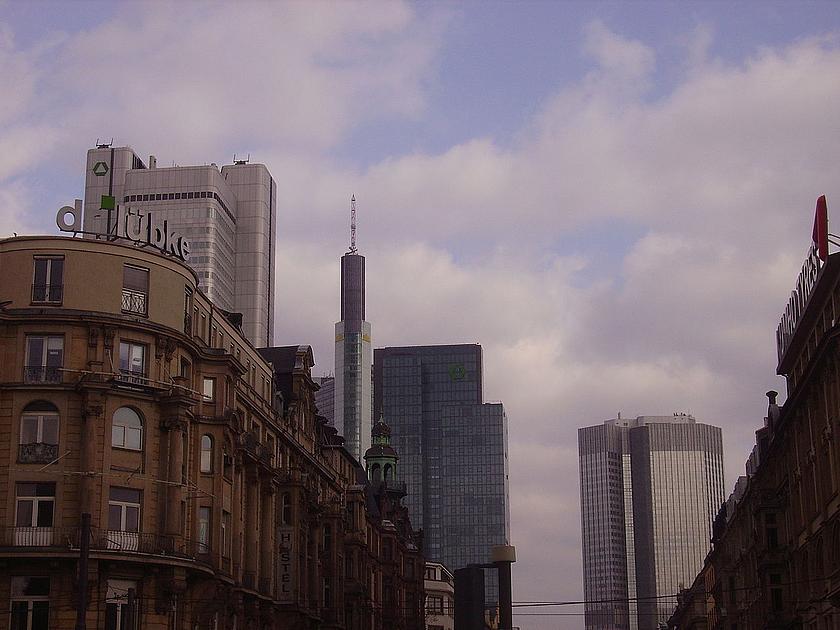 Blick von einem Straßenzug in Frankfurt am Main auf Drei Hochhäuser im Hintergrund.