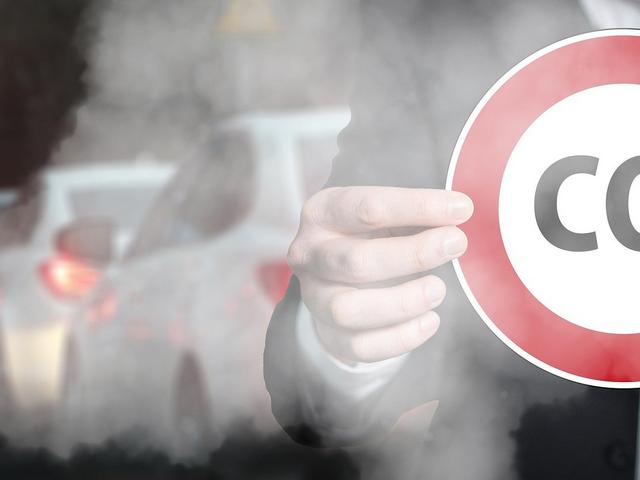 Stop-CO2-Schild, im Hintergrund Abgase vom Verkehr