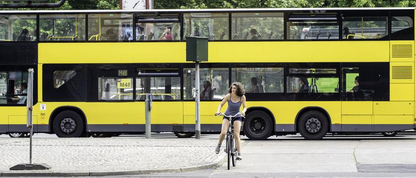 Im Vordergrund eine Frau auf einem Fahrrad und im Hintergrund ein gelber Linienbus
