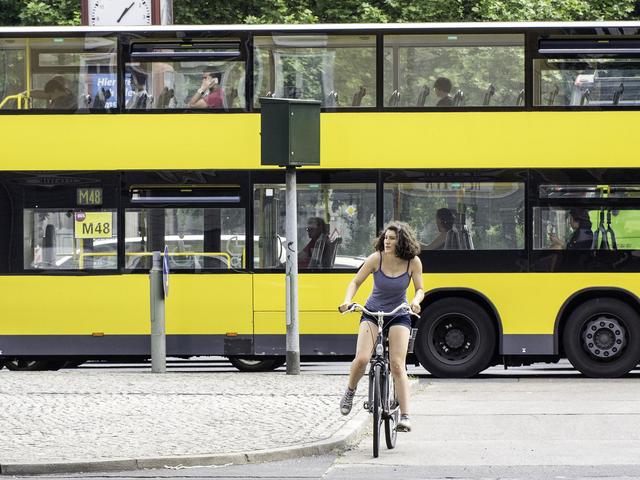 Im Vordergrund eine Frau auf einem Fahrrad und im Hintergrund ein gelber Linienbus