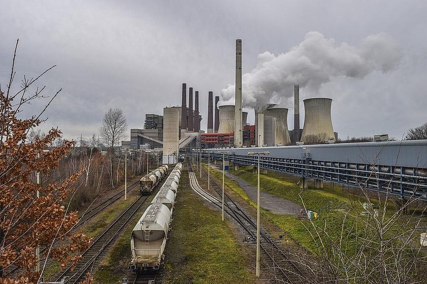 Ein Kohlekraftwerk im Hintergrund, mit Kohletransportern auf Schienen im Vordergrund.
