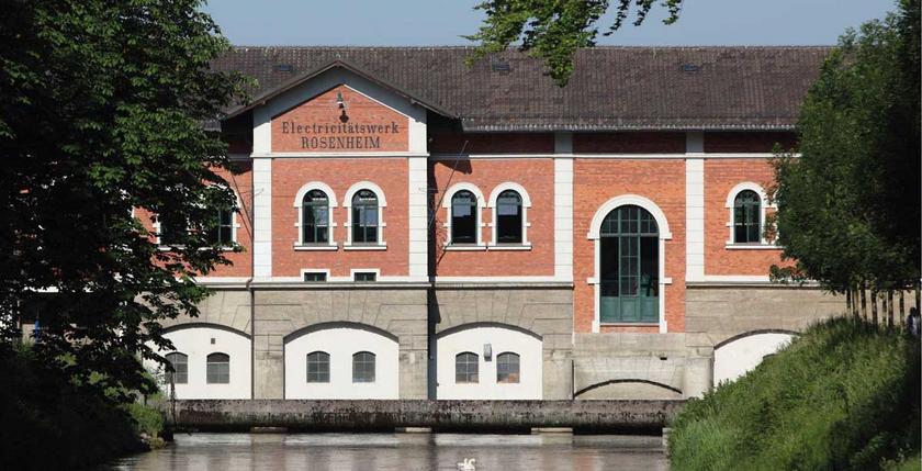 Wasserkraftwerk Rosenheim: rotgeklinkerte Fassade, davor der Fluss
