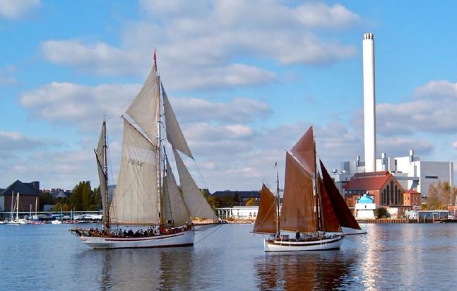 Zwei Segelboote, im Hintergrund ein Industriegebäude mit Schornstein, die Stadtwerke Flensburg