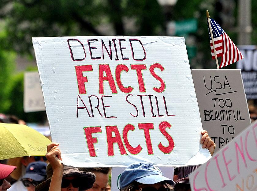 Plakat auf einer Demonstration mit der Aufschrift: denied facts are still facts. Zu deutsch: geleugnete Fakten sind immer noch Fakten.