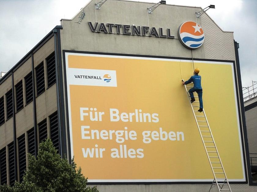 Hauswand eines Berliner Altbaus mit der Aufschrift „Vattenfall, für Berlins Energie geben wir alles“, eine Figur aus Pappmaché erklimmt eine Leiter, die an eben dieser Hauswand lehnt.