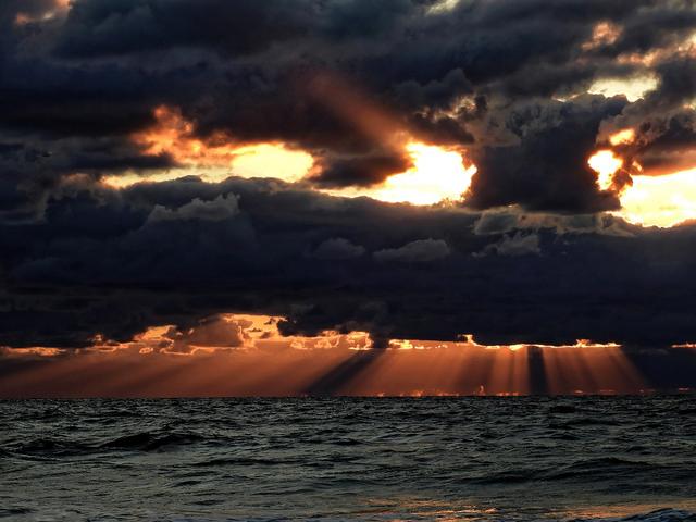 Das Meer und darüber Wolken und Sonne am Abend.