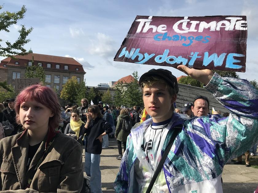 Zwei Jugendliche auf einer Demo. Einer hält ein Plakat hoch auf dem steht: "The Climate changes, why don´t we"