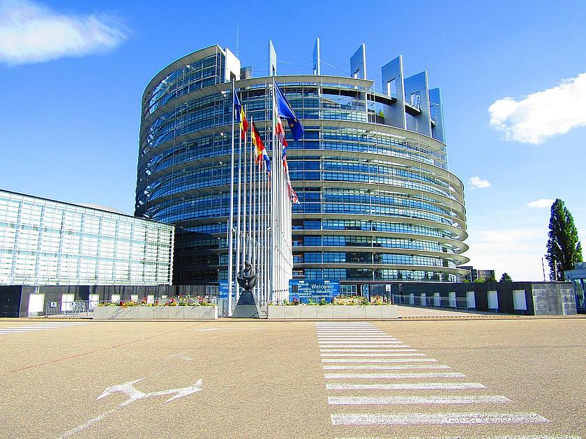 Sitz des EU-Parlaments in Straßburg mit Fahnen der EU-Mitgliedsstaaten davor.