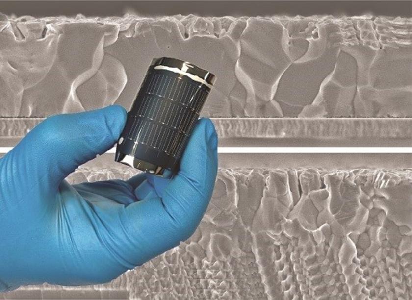 Hand hält gerollte flexible Solarzelle, im Hintergrund Mikroskopaufnahme Schichtaufbau