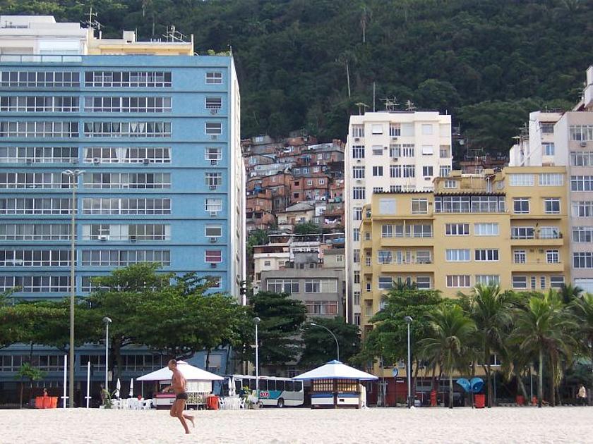 Am Strand von Rio mit Blick auf die Stadt. Direkt am Strand befinden sich hohe feine Häuser. Im Hintergrund ist die Favela mit kleinen Häusern zu sehen.