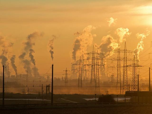 Industrieanlagen mit rauchenden Schloten und Strommasten im Sonnenaufgang