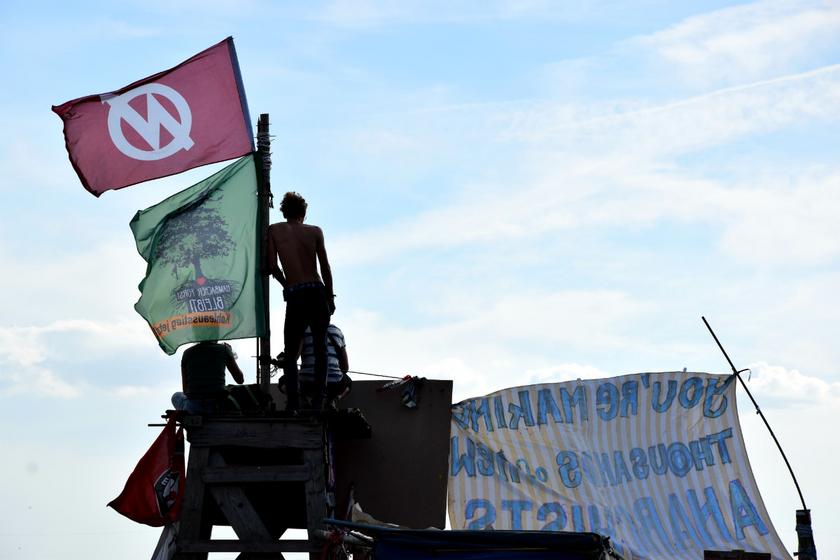 Aktivist:innen aus dem Hambacher Wald stehen auf einem Campgebäude mit einer Fahne "Hambi bleibt"