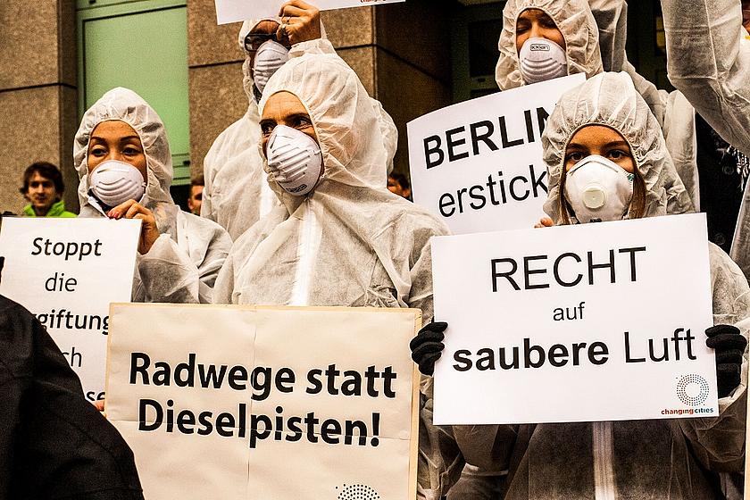 Demonstranten mit Atemschutzmasken und Schildern auf denen steht: "Recht auf saubere Luft" und "Radwege statt Dieselpisten".