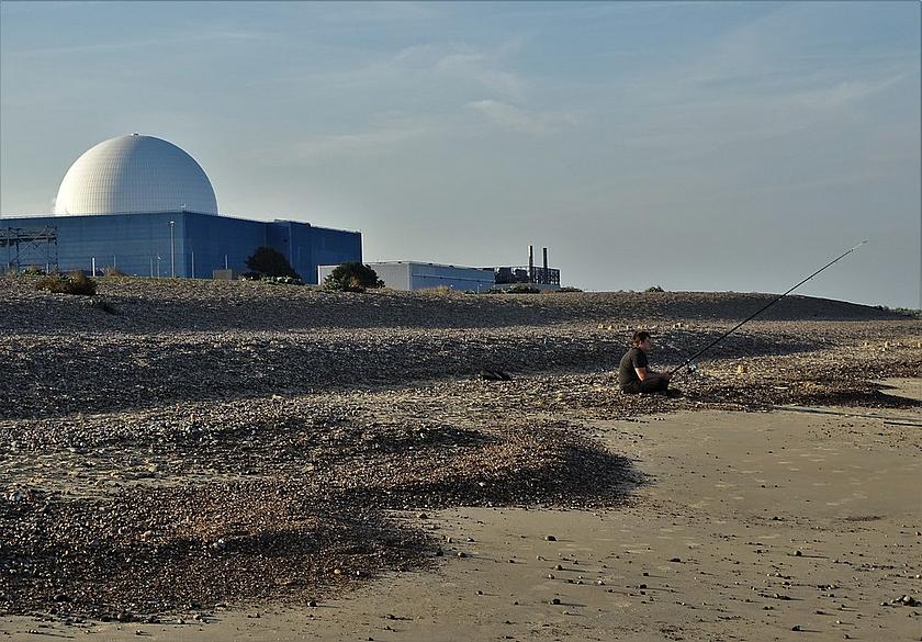 Ein Fischer sitzt am Strand. Hinter ihm erhebt sich ein Atomkraftwerk