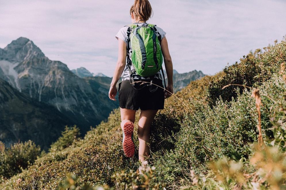 Eine Frau mit Rucksack, von hinten zu sehen geht in den Bergen Wandern