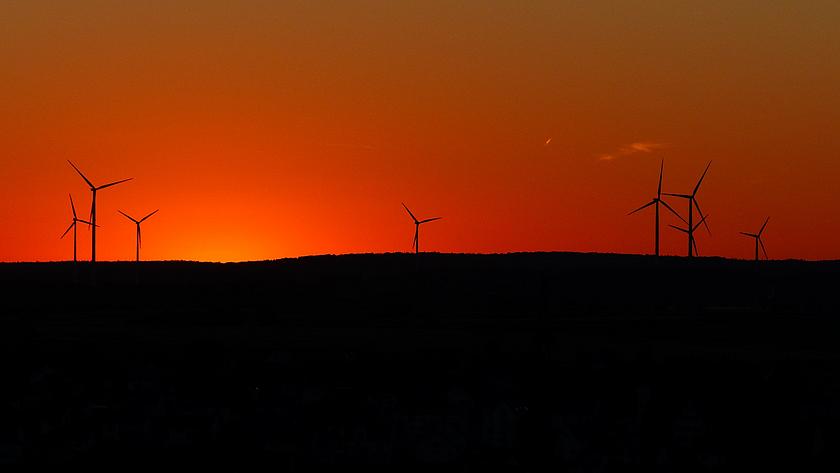 Windräder am Horizont auf einem Hügel im Sonnenuntergang.