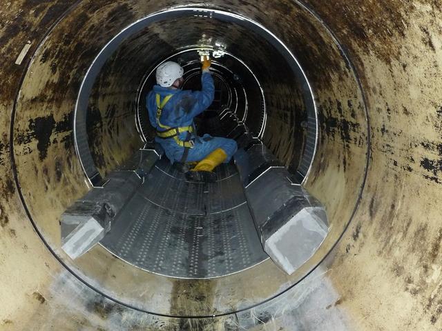 Ein Arbeiter sitzt in einem unterirdischen Kanal und installiert etwas metallenes