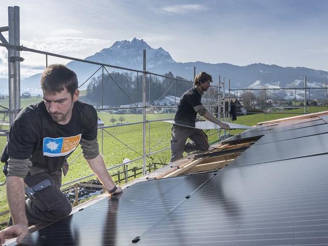 Zwei Männer montieren Solaranlage, im Hintergrund Berge, die Alpen
