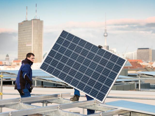 Ein Mann trägt ein Solarmodul auf einem Dach