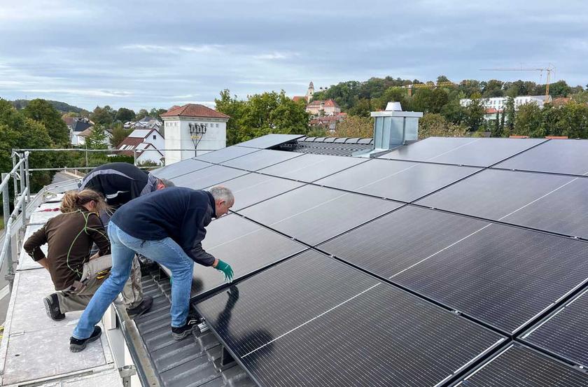 Drei Menschen installieren PV-Anlage auf Hausdach