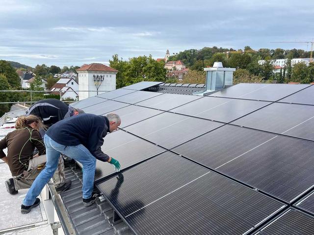 Drei Menschen installieren PV-Anlage auf Hausdach
