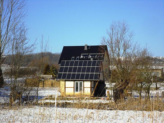 Kleines Haus in Winterlandschaft mit Solaranlage auf dem Dach.