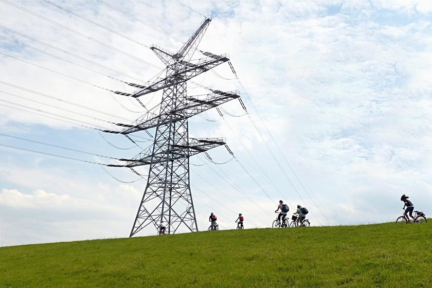 Strommast mit Stromnetz auf grünem Hügel, darunter eine Gruppe Fahrradfahrer