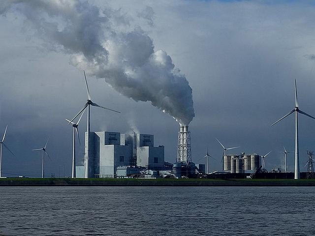 Ein Kohlekraftwerk am Wasser, umgeben von Windrädern